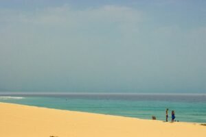 a couple of people standing on top of a sandy beach